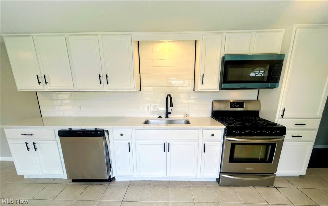 558 Lessig Avenue Akron, OH 44312 - Photo 7 of 15 Kitchen with stainless steel appliances, white cabinets, light stone countertops, tasteful backsplash, and light tile patterned floors