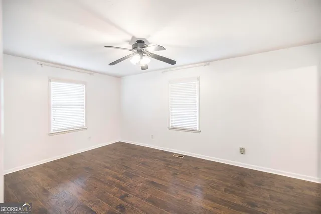 an empty room with wooden floor fan and windows