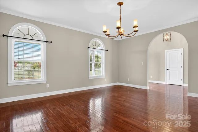 an empty room with wooden floor chandelier and a window