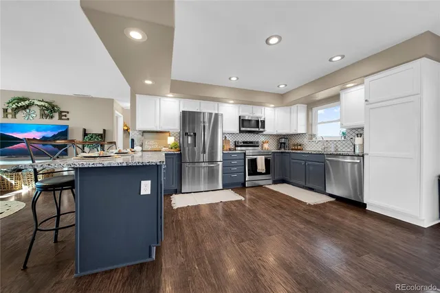 a kitchen with stainless steel appliances granite countertop a refrigerator a stove top oven a sink dishwasher and white cabinets with wooden floor