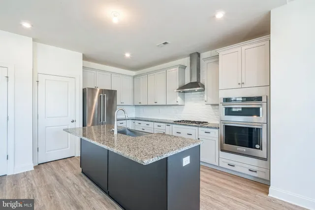 a kitchen with stainless steel appliances granite countertop a stove a refrigerator a sink and white cabinets with wooden floor