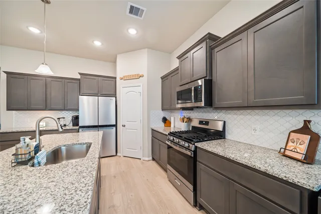 a kitchen with stainless steel appliances granite countertop a sink a stove top oven a refrigerator with wooden cabinets and floor