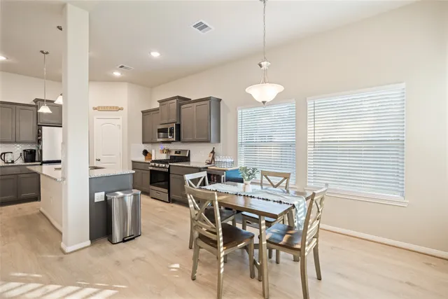 a kitchen with stainless steel appliances kitchen island granite countertop a stove a refrigerator a sink a dining table and chairs with wooden floor