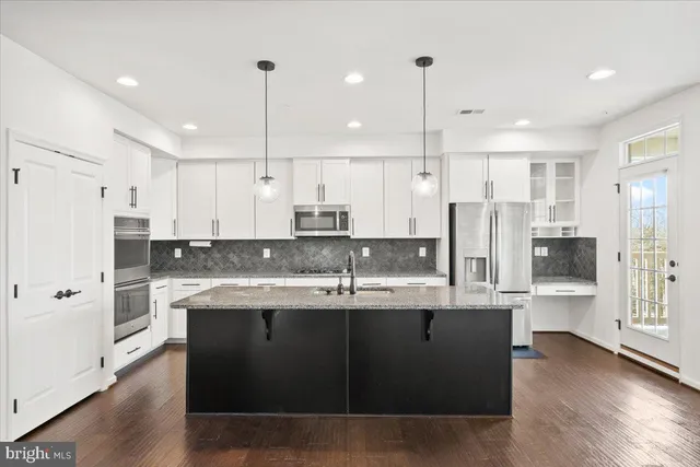 a kitchen with stainless steel appliances granite countertop a refrigerator a sink dishwasher a stove and white cabinets with wooden floor