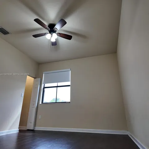 an empty room with wooden floor fan and windows
