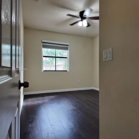 an empty room with wooden floor chandelier fan and windows