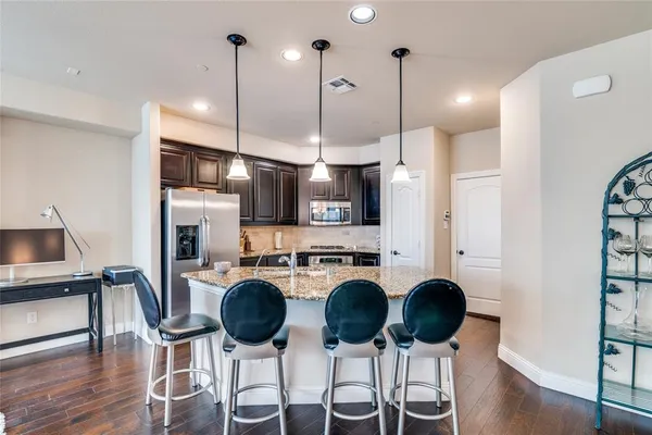 a kitchen with stainless steel appliances kitchen island granite countertop a refrigerator a stove a kitchen island a dining table and chairs with wooden floor