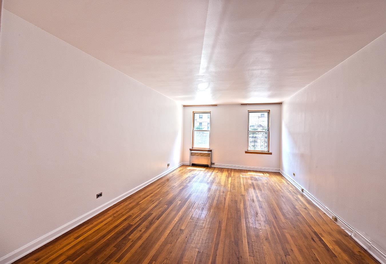 a view of an empty room with wooden floor and window