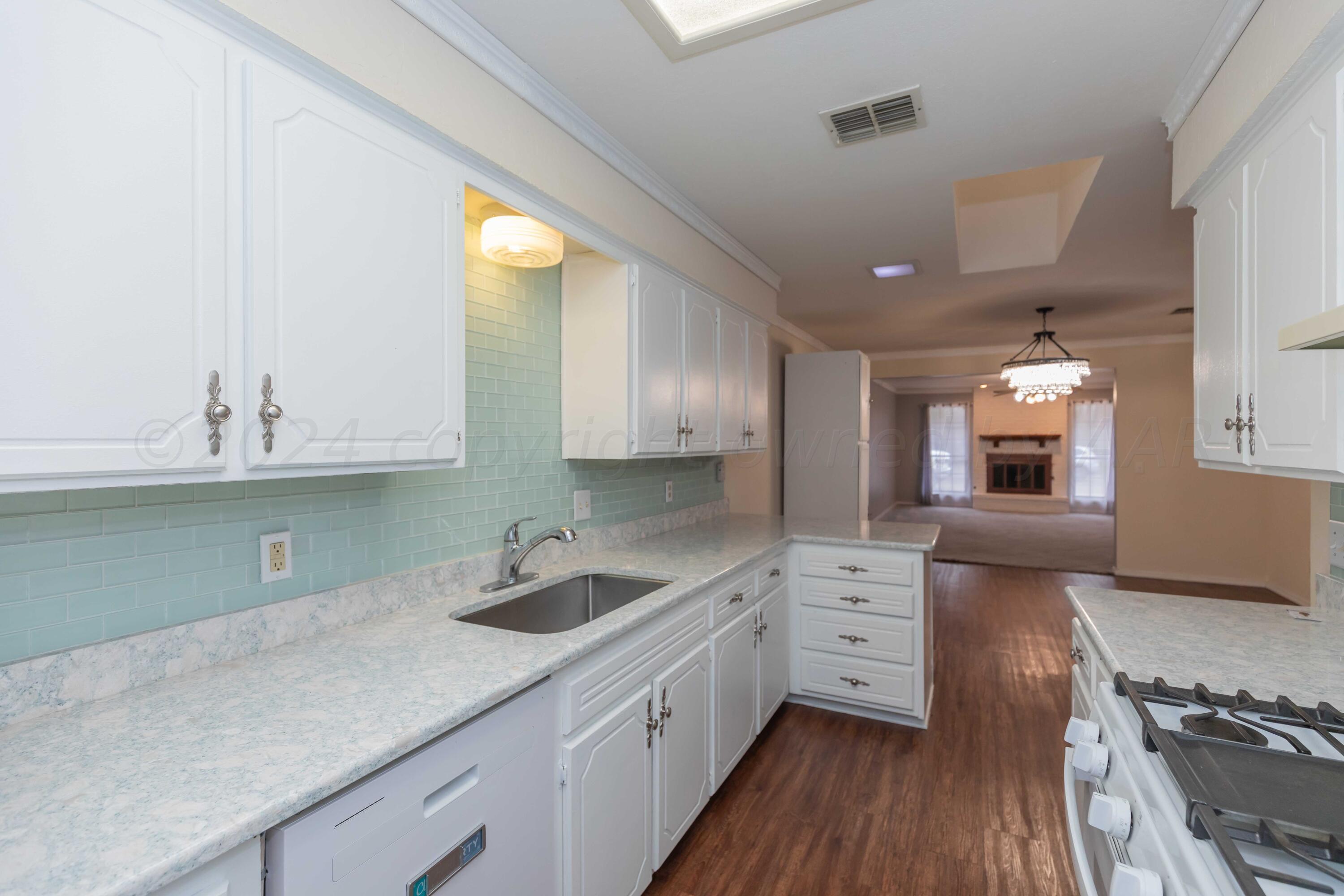 3406 Gladstone Lane Amarillo, TX 79121 - Photo 12 of 35 a kitchen with a sink dishwasher a stove and white cabinets with wooden floor