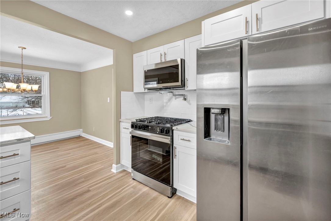 1447 East Sprague Road Independence, OH 44131 - Photo 11 of 47 Kitchen featuring tasteful backsplash, white cabinetry, hanging light fixtures, stainless steel appliances, and light hardwood / wood-style flooring
