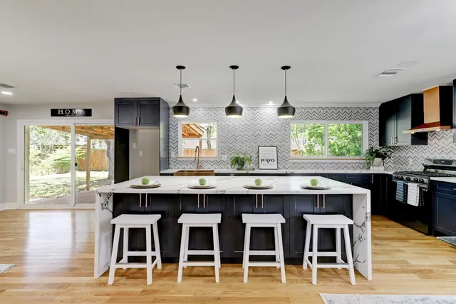 a large kitchen with granite countertop a stove a sink a dining table and chairs with wooden floor