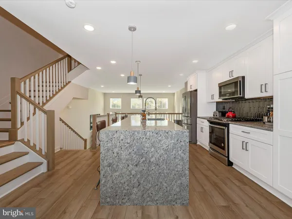 a kitchen with stainless steel appliances kitchen island granite countertop a refrigerator oven a sink dishwasher and white cabinets with wooden floor