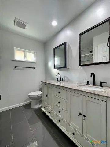 a spacious bathroom with double sink a toilet and a mirror