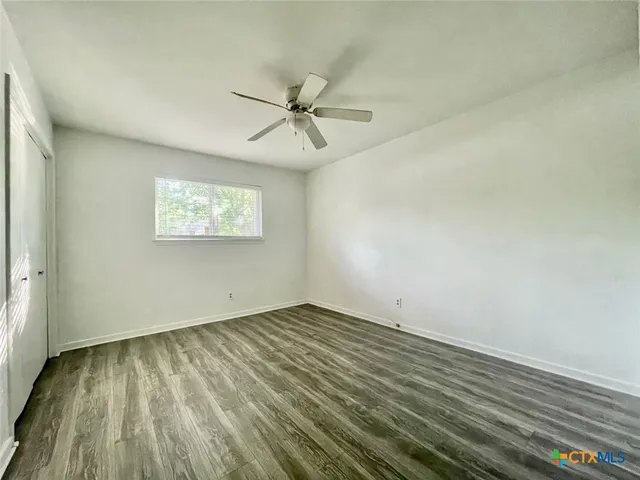 an empty room with wooden floor fan and windows