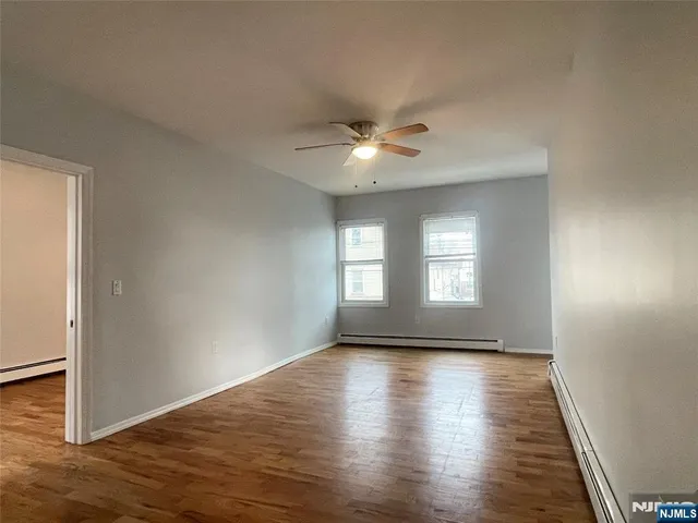 a view of empty room with wooden floor and fan
