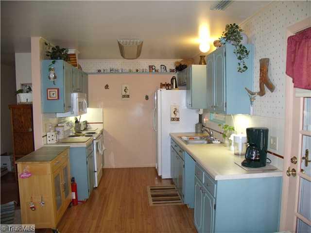 Kitchen. New laminate flooring in kitchen & dining area.  Tile backsplash. Under cabinet lighting. Area open to LR. Door to screened back porch.  (Small brown cabinet to left does not convey).