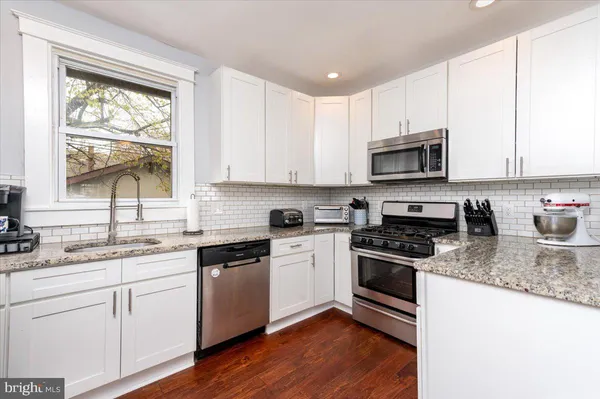 a kitchen with kitchen island granite countertop a sink cabinets stainless steel appliances and a window