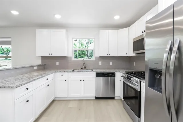 a kitchen with granite countertop white cabinets stainless steel appliances a sink and a window