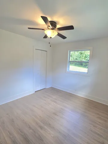 an empty room with wooden floor fan and windows