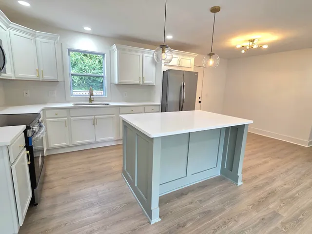 a kitchen with kitchen island a sink dishwasher a stove and white cabinets with wooden floor