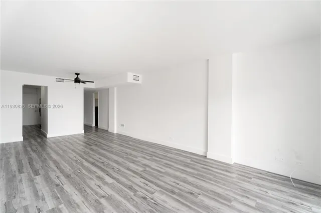 a view of an empty room with wooden floor and a ceiling fan
