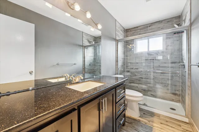 a bathroom with a granite countertop sink a toilet a mirror and shower