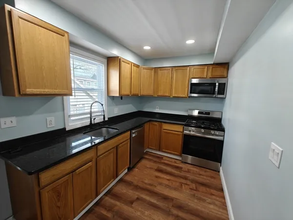 a kitchen with stainless steel appliances granite countertop wooden cabinets a stove a sink and a microwave