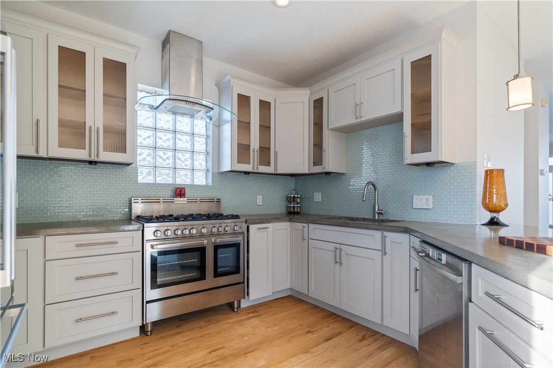 711 University Road Cleveland, OH 44113 - Photo 13 of 36 Kitchen featuring wall chimney exhaust hood, sink, light wood-type flooring, pendant lighting, and stainless steel appliances