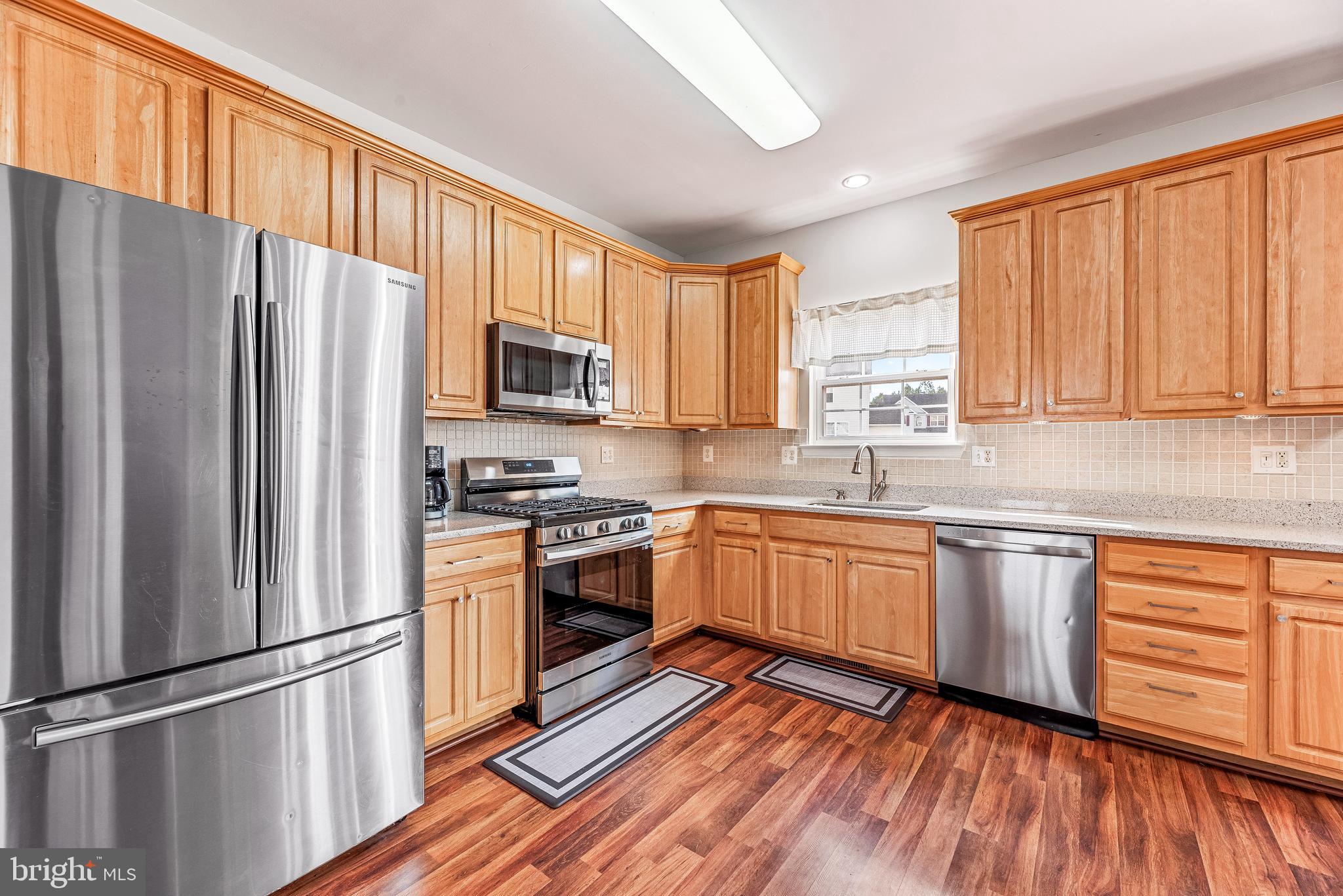 a kitchen with granite countertop wooden floors stainless steel appliances and window