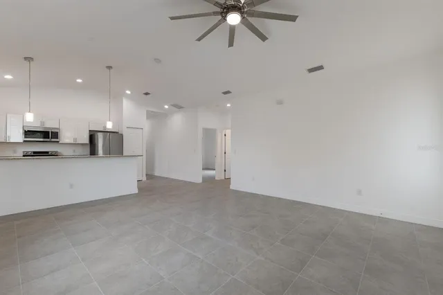 a view of an empty room with kitchen appliances and a ceiling fan
