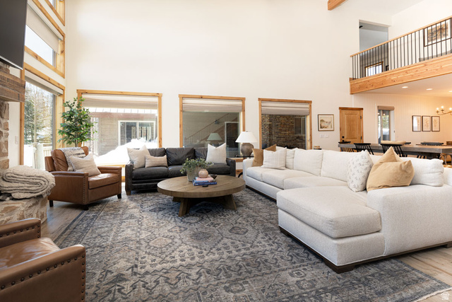 382 Ridgeview Street, Unit 8 & 9 Brian Head, UT 84719 - Photo 9 of 52 Spacious living area featuring double-height ceilings, large windows with natural wood trim, wood-finish flooring, a stone-clad fireplace, and an open-concept layout with a visible second-story overlook