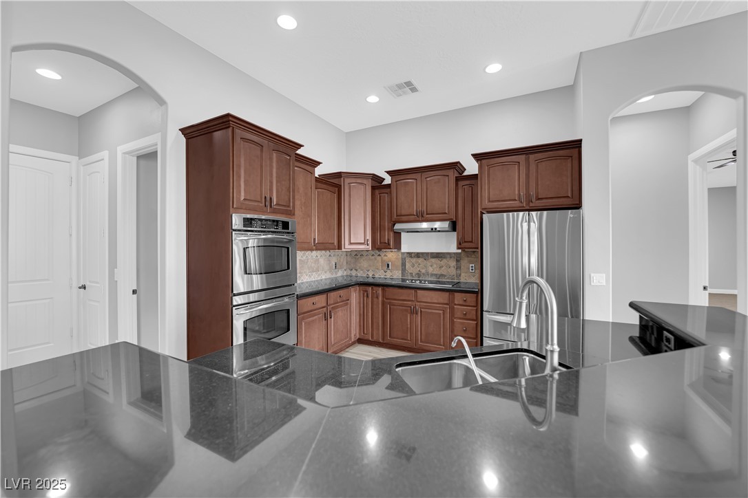 1415 Curohee Street Moapa, NV 89025 - Photo 10 of 54 Kitchen with arched walkways, appliances with stainless steel finishes, tasteful backsplash, dark stone countertops, and recessed lighting
