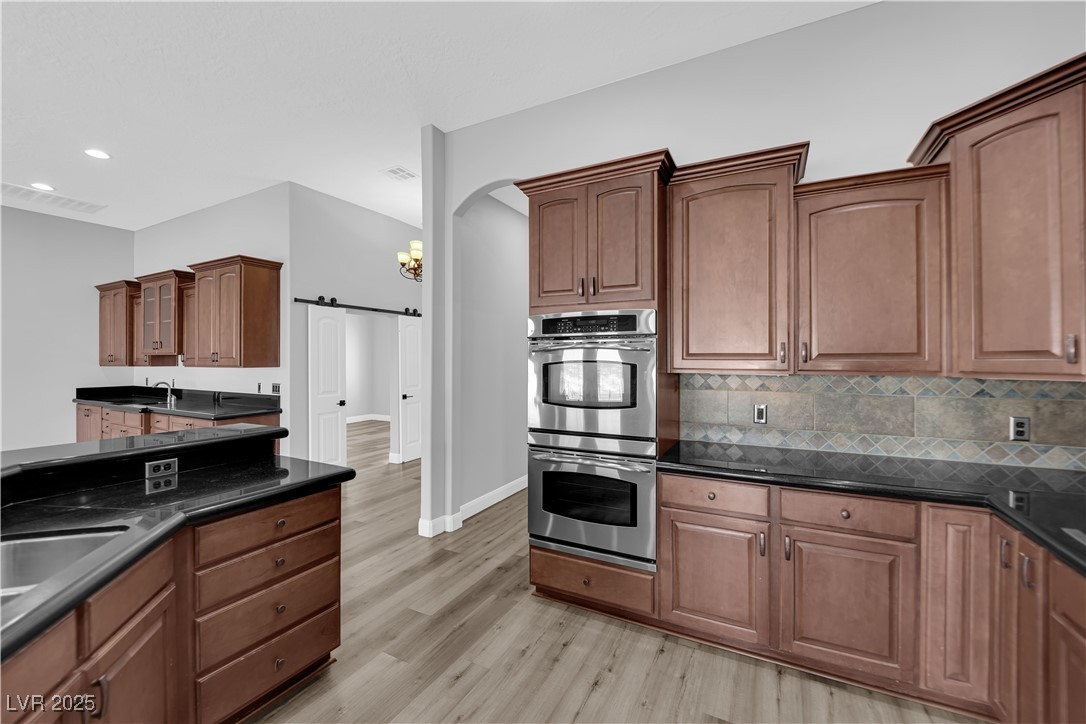 1415 Curohee Street Moapa, NV 89025 - Photo 12 of 54 Kitchen with stainless steel double oven, a barn door, tasteful backsplash, arched walkways, and light wood-style flooring