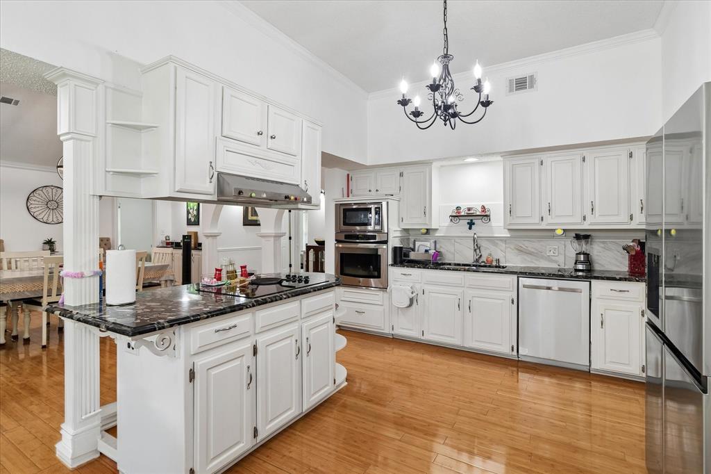 3007 McReynolds Road Sanger, TX 76266 - Photo 6 of 39 Kitchen featuring a central island with cooktop, white cabinetry, dark stone countertops, wood-finish flooring, and stainless steel appliances including a built-in oven and microwave