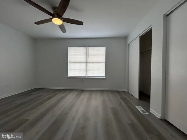 an empty room with wooden floor ceiling fan and windows