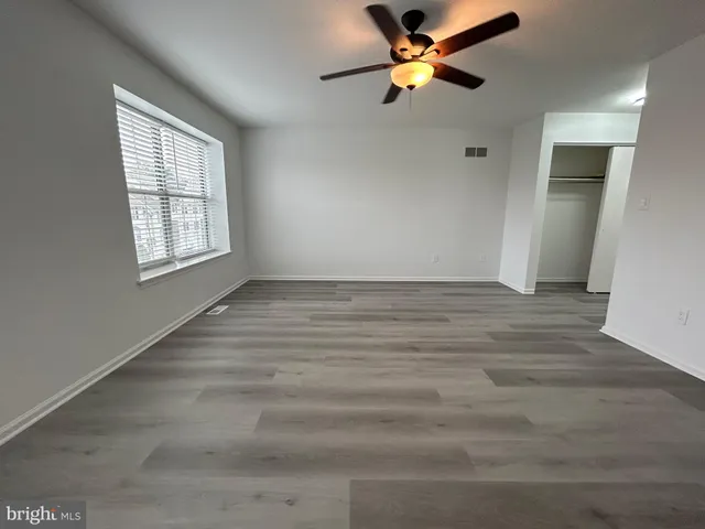 an empty room with wooden floor fan and windows