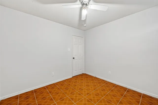 an empty room with a chandelier fan and wooden floor