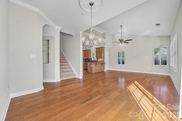 a view of an empty room with wooden floor and a kitchen