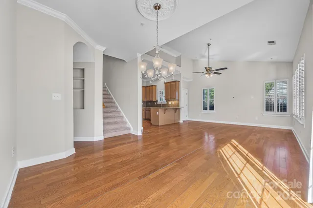 a view of an empty room with wooden floor and a kitchen