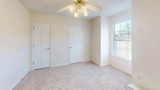 an empty room with chandelier fan and windows