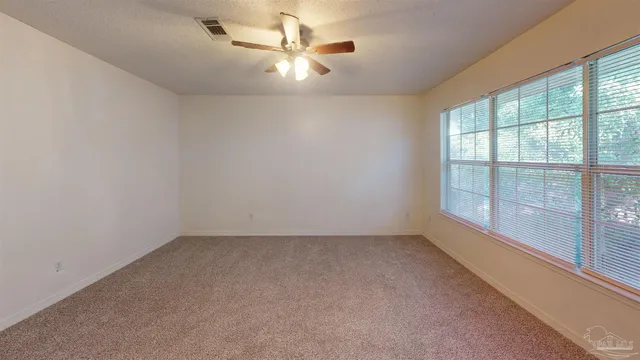 an empty room with chandelier fan and windows