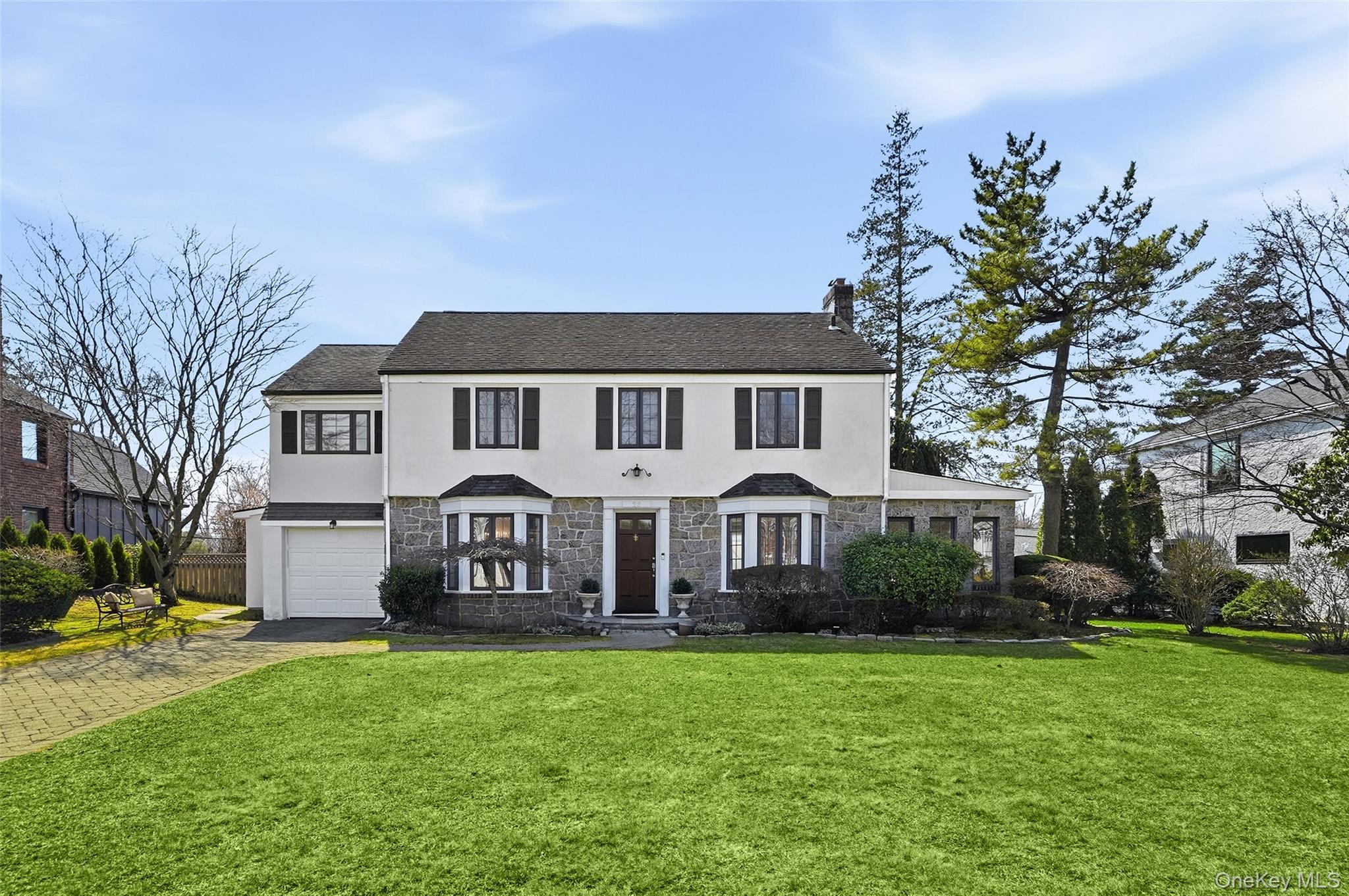 View of front of house featuring stone and stucco siding, garage, paver driveway and a front lawn.