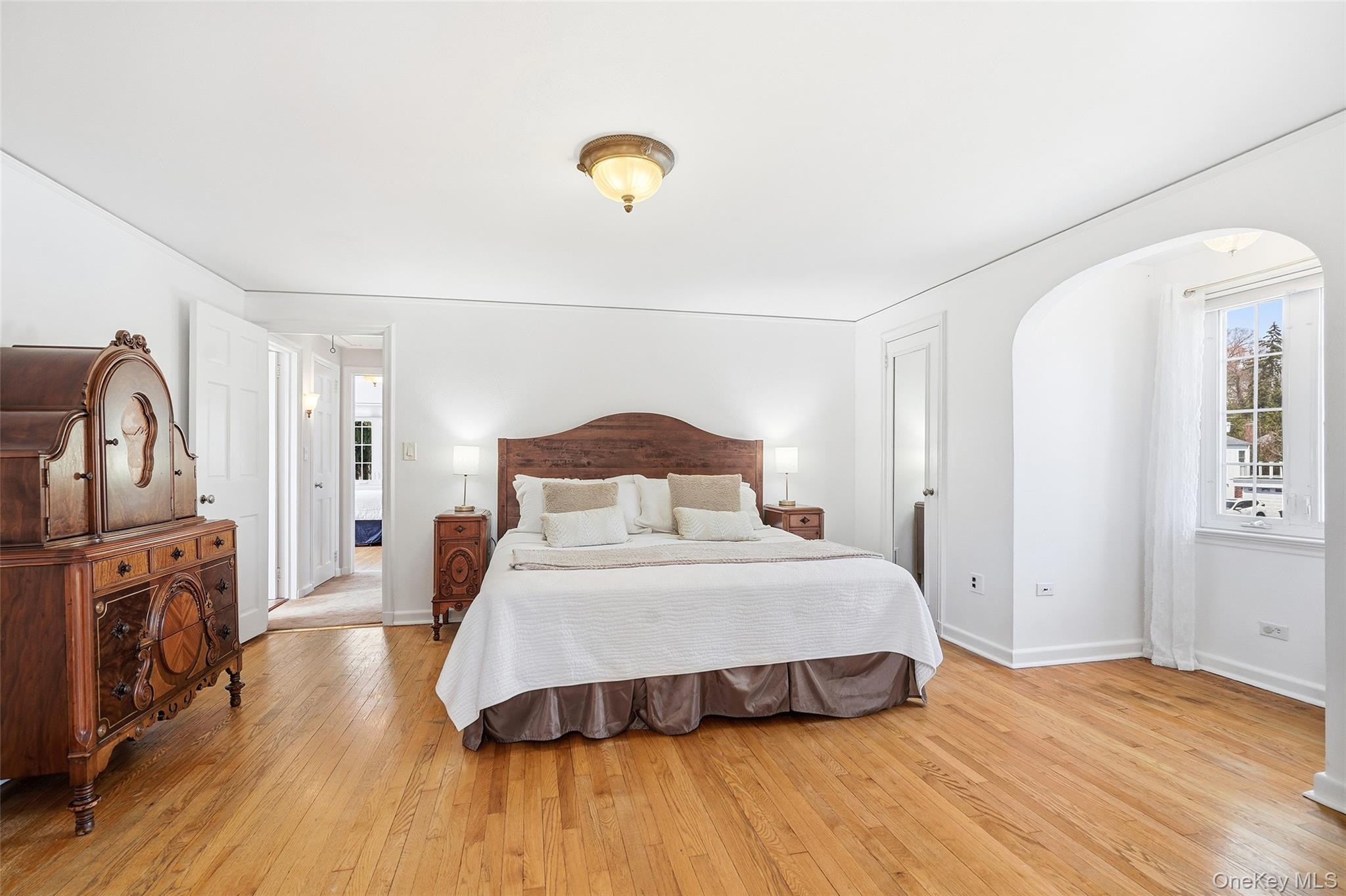 42 Sargent Road Scarsdale, NY 10583 - Photo 14 of 27 Spacious primary bedroom with rich hardwood flooring, double closets, and a charming arched alcove framed by windows.