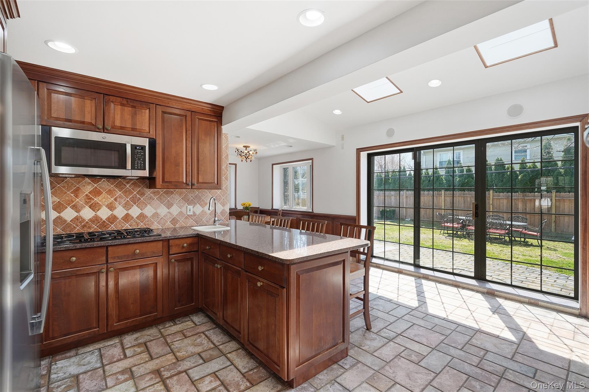 42 Sargent Road Scarsdale, NY 10583 - Photo 7 of 27 Open and bright Kitchen with expansive glass doors to the backyard, kitchen bar, a peninsula, granite countertops, stainless steel and black appliances, and wood finish cabinets.