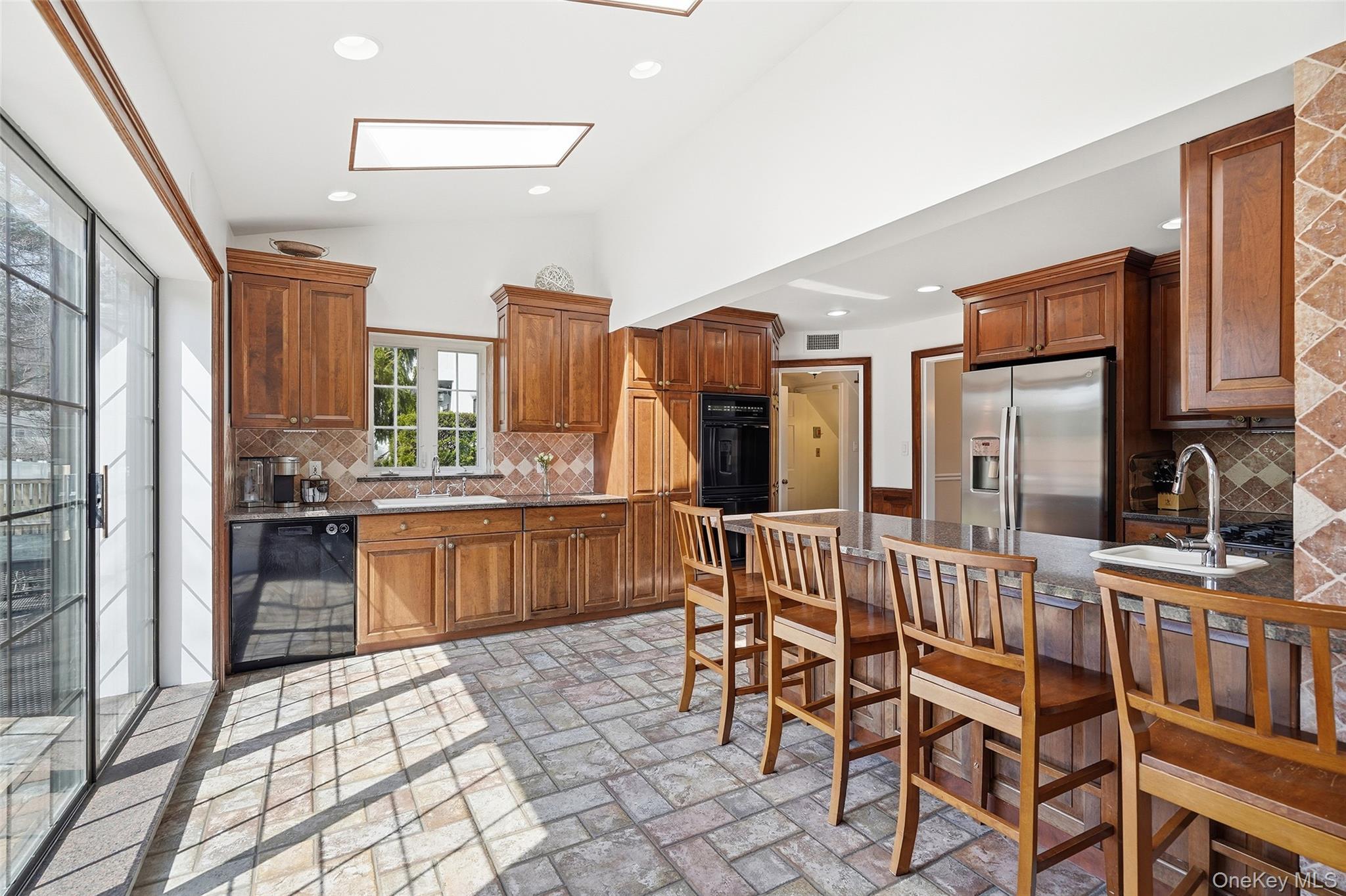 42 Sargent Road Scarsdale, NY 10583 - Photo 9 of 27 Kitchen with tasteful backsplash, granite countertops, stainless steel and black appliances, a breakfast bar, and wood finish cabinets.