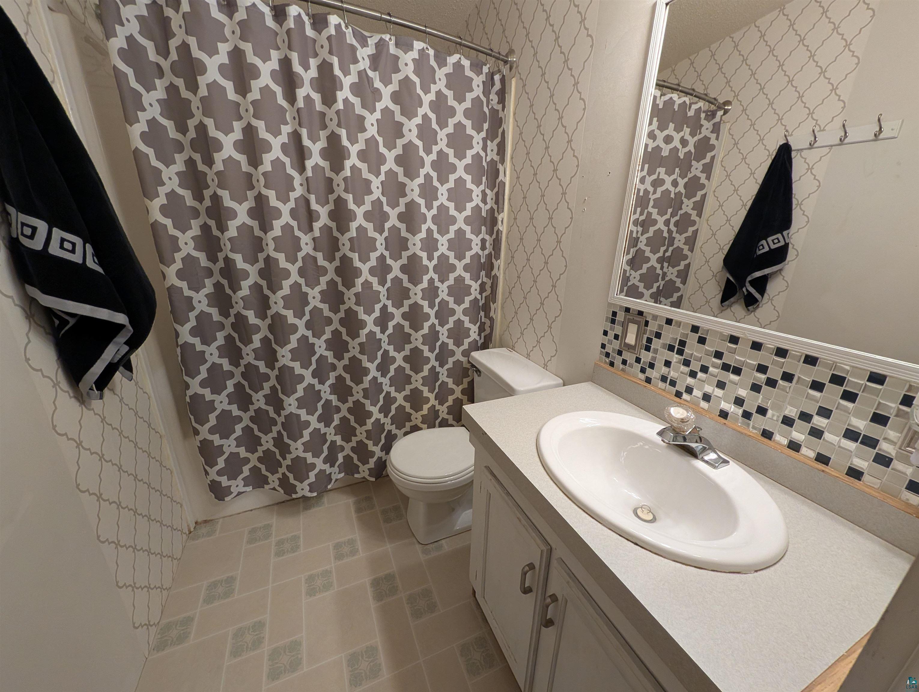 3945 Maple Street Kettle River, MN 55757 - Photo 30 of 41 Bathroom featuring a vanity with an integrated sink, a rectangular mirror, and a mosaic tile backsplash