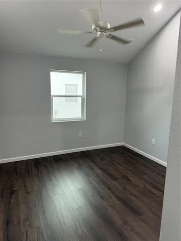 an empty room with wooden floor fan and windows