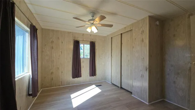 an empty room with wooden floor fan and windows