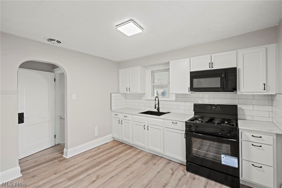 1218 Briggle Road Akron, OH 44320 - Photo 13 of 40 Contemporary kitchen featuring white cabinetry with black hardware, wood-finish flooring, subway tile backsplash, white countertops, and a black gas range