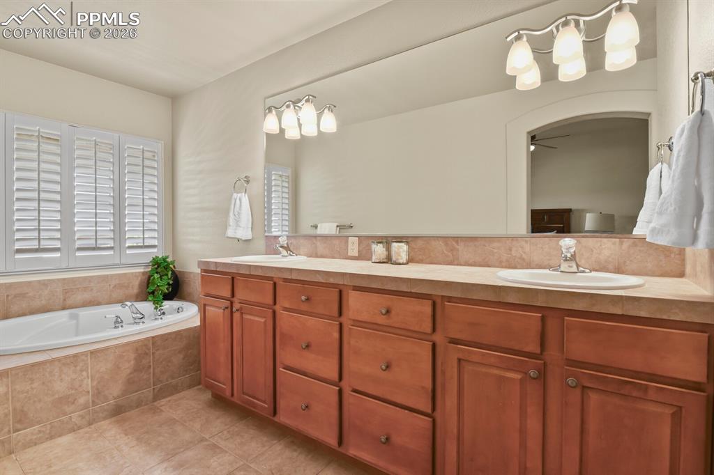 617 Concerto Drive Colorado Springs, CO 80906 - Photo 20 of 46 Bathroom featuring a large corner soaking bathtub, wood vanity with two sinks, and a vanity mirror with overhead lighting